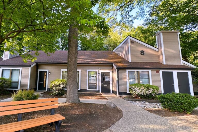 exterior of new jersey addiction treatment center. brown building surrounded by mature trees, mulch landscaping, concrete walkway leading to the door